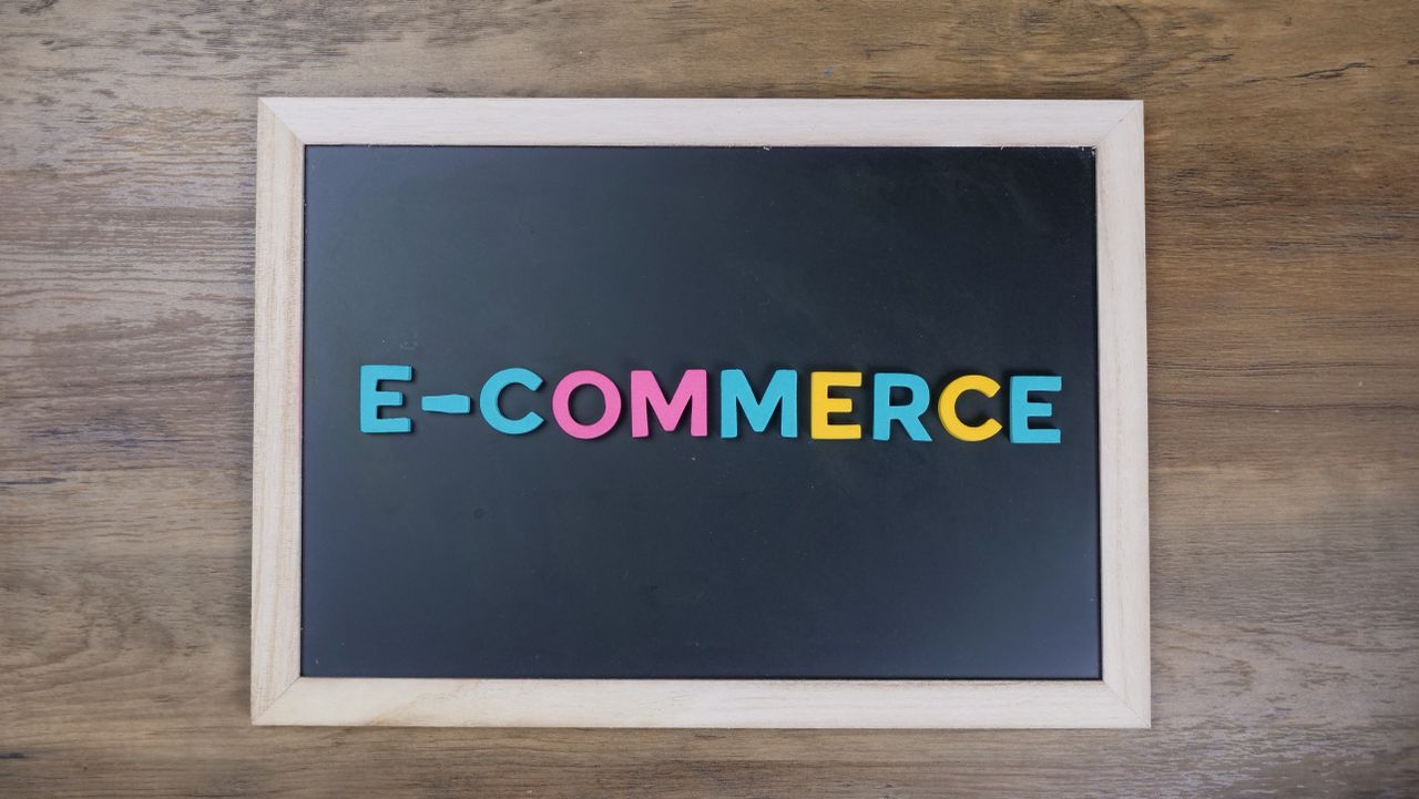 Lettres colorées formant le mot e-commerce sur un tableau noir encadré de bois.